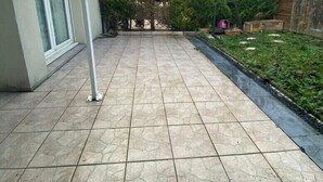 Um pátio com piso de azulejos, cercado por árvores e uma cerca de madeira.