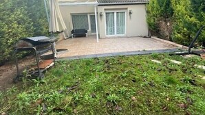Uma casa com um pátio, uma área coberta para sentar e um pequeno jardim.
