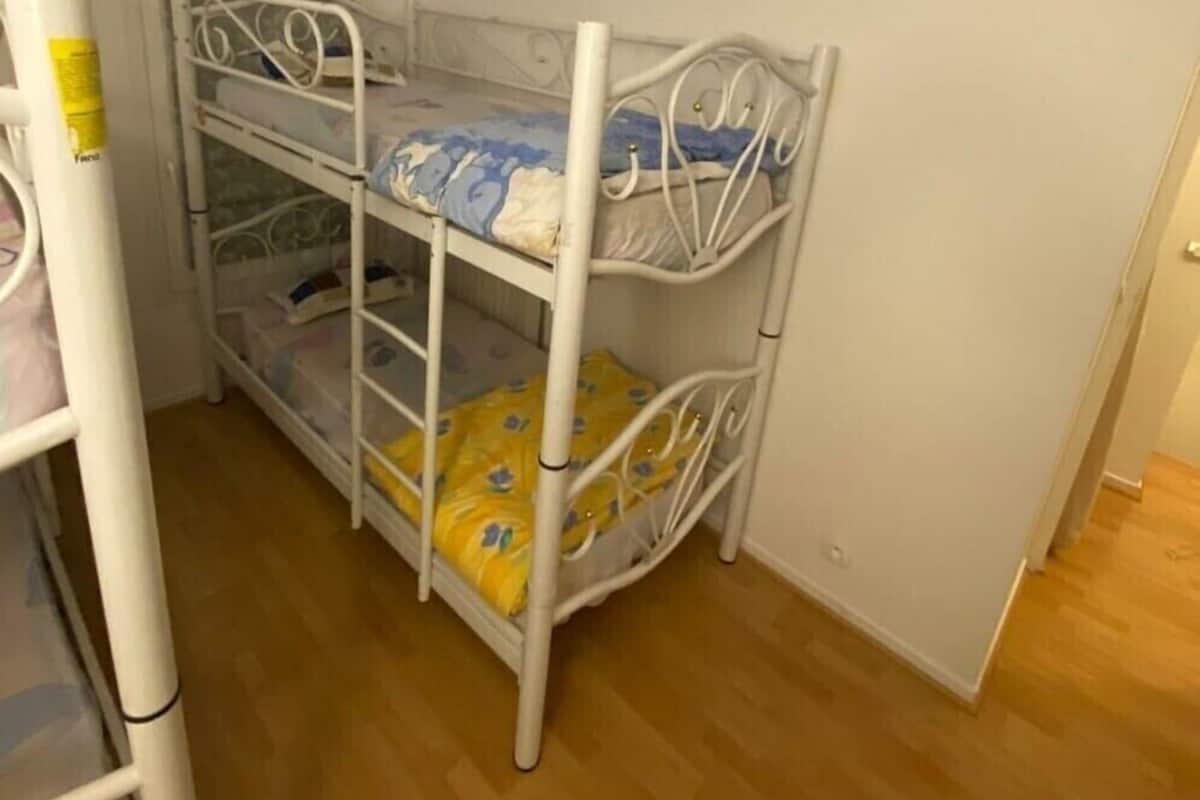 A bunk bed room with three levels, white metal frame, and a wooden floor.