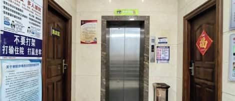 A hotel lobby with a marble floor, a reception desk, and a sign indicating the elevator area.