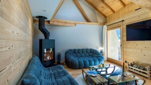 Un interior de cabaña acogedor, con paredes de madera, un estufa de leña empotrada, un sofá azul, una mesa de centro de cristal y una estantería de piedra para vinos.
