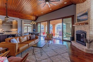 A spacious living area with a wooden ceiling, a fireplace, and a large window offering a view of the outdoors.