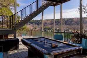 A pool table with a railing and a staircase on a deck overlooking a forested area.