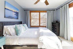 A bedroom with a bed, a nightstand, a dresser, a ceiling fan, and a window with curtains.