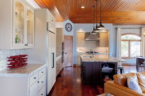 A spacious kitchen with wooden ceiling, a central island, and a dining area with a leather couch.