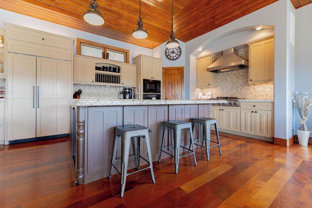 Una cocina moderna con una isla central, taburetes de bar, piso de madera y un reloj en la pared.