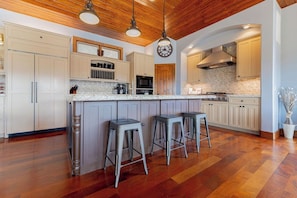 Une cuisine dotée d’un îlot central, de tabourets de bar, d’un plancher en bois et d’une horloge au mur.