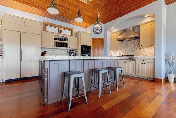 A modern kitchen with a central island, bar stools, wooden flooring, and a clock on the wall.