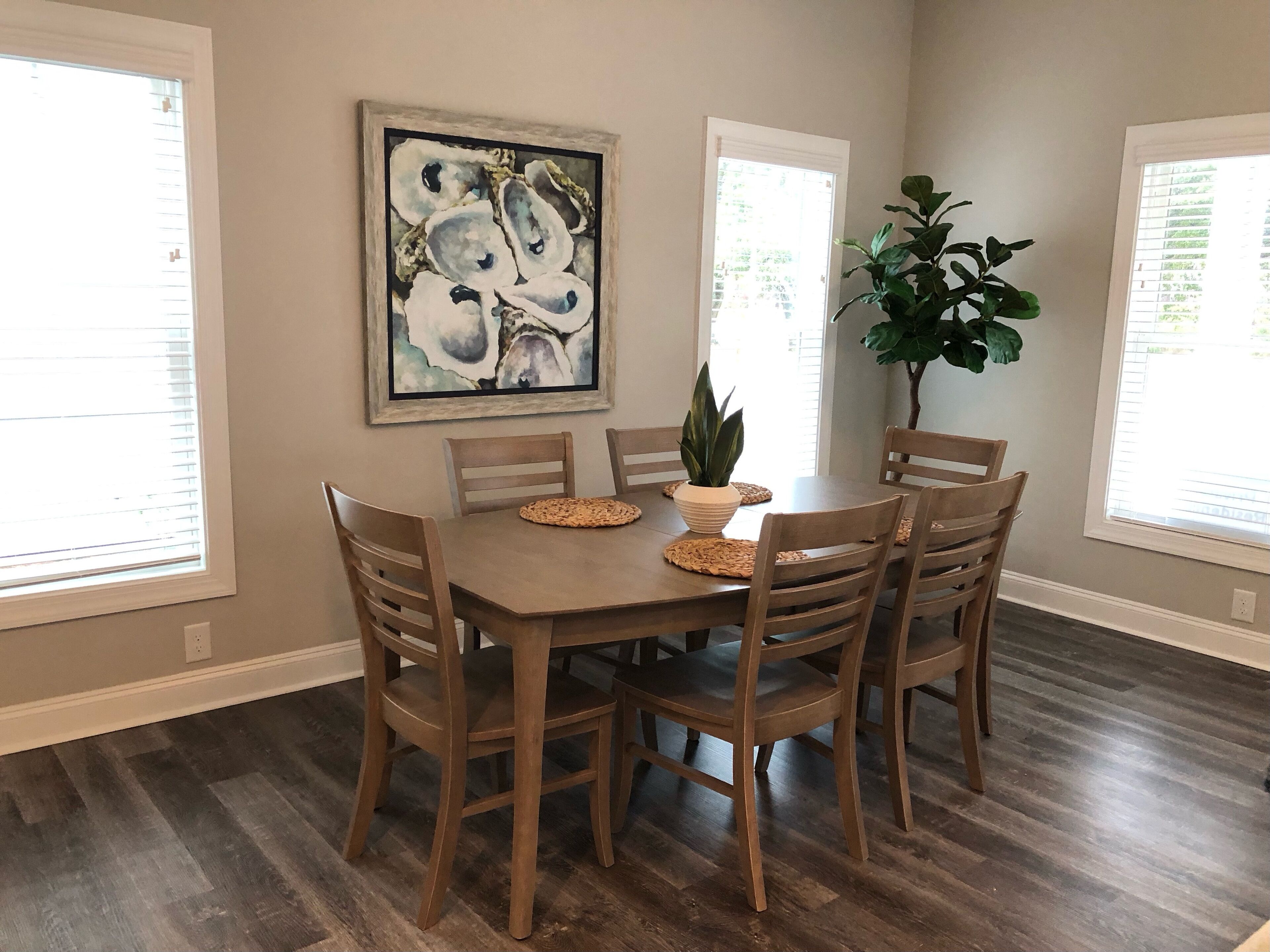 A dining area with a wooden table and chairs, a potted plant, and a framed artwork on the wall.