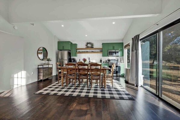 A modern kitchen with green cabinets, a dining area with a checkered rug, and a large window with a view.