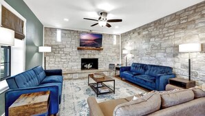 A living room with a stone wall, a fireplace, blue sofas, and a ceiling fan.