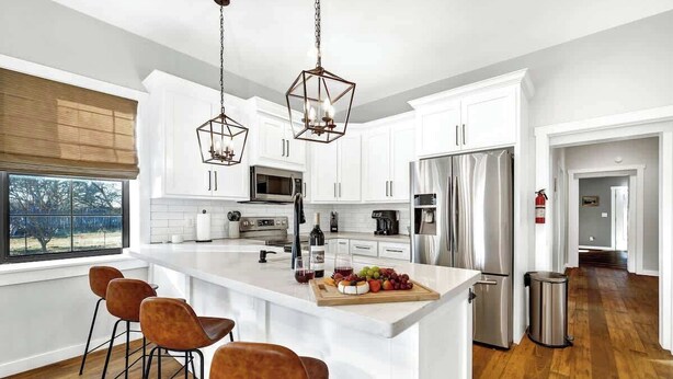 A modern kitchen with white cabinets, a central island with bar stools, stainless steel appliances, and pendant lighting.