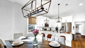 A modern kitchen with white cabinets, a wooden dining table set for four, and pendant lights.