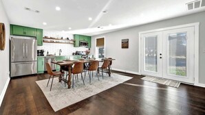 A modern kitchen with green cabinets, a stainless steel refrigerator, and a dining area with a wooden table and chairs. - Waylons House+Hot Tub+Party Barn (Fredericksburg)