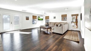 A spacious living room with a dark hardwood floor, a beige sofa, and a coffee table. - Waylons House+Hot Tub+Party Barn (Fredericksburg)
