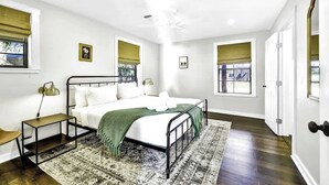 A bedroom with a bed, bedside tables, a ceiling fan, and windows with blinds. - Waylons House+Hot Tub+Party Barn (Fredericksburg)