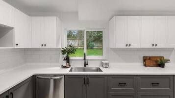 A modern kitchen with white cabinets, a stainless steel sink, and a view of a backyard through a large window.