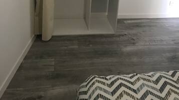 Een inloopkast met hangruimte en planken, een bed met een bedovertrek met dessin, en een houten vloer.