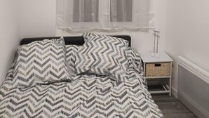 A bedroom with a bed, a nightstand, a window with sheer curtains, and a radiator. - residence romi entire accommodation 4 people (Tillé)