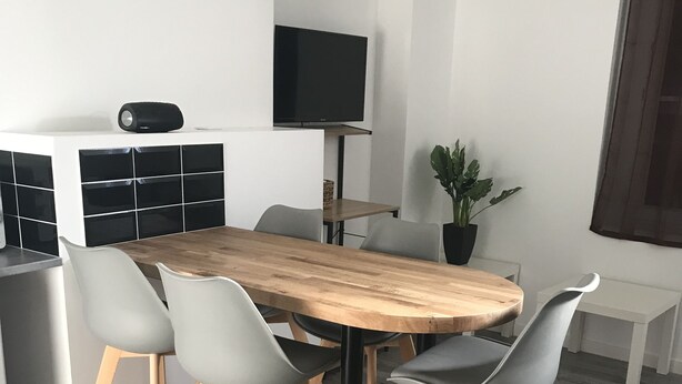 A modern dining area with a wooden table and four grey chairs. A flat-screen TV is mounted on the wall above the table. - residence romi entire accommodation 4 people (Tillé)