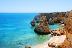 Eine Küstenlandschaft mit klarem türkisblauem Wasser, Felsformationen und einem Sandstrand.