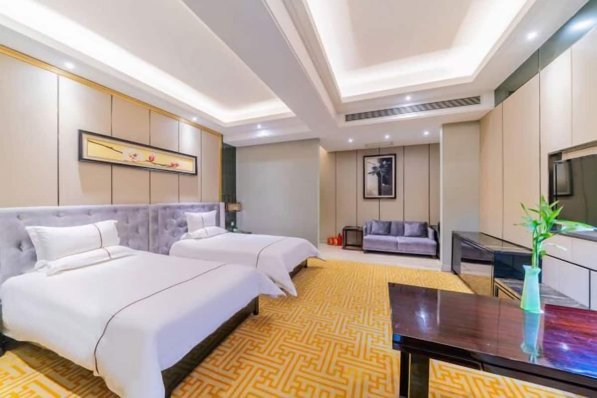 Una habitación de hotel con dos camas, un sofá, un televisor y un jarrón decorativo.