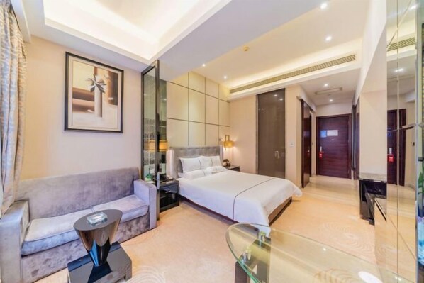 A modern hotel room with a large bed, a sofa, a glass coffee table, and a bedside table with a lamp. - Jia Ye Hotel (Dongguan)