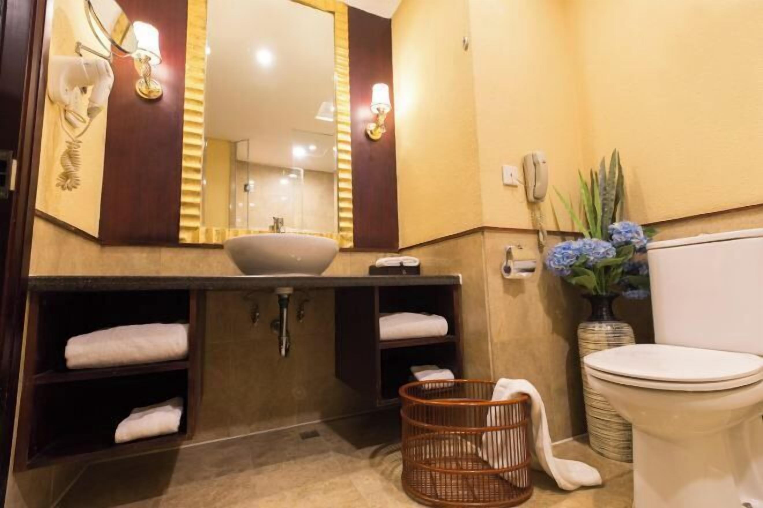 Een badkamer met een grote spiegel, een wastafel, een toilet en een rieten mand.