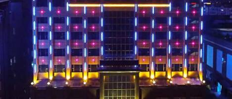 Un hôtel à plusieurs étages, doté d’une entrée imposante et d’une enseigne lumineuse.