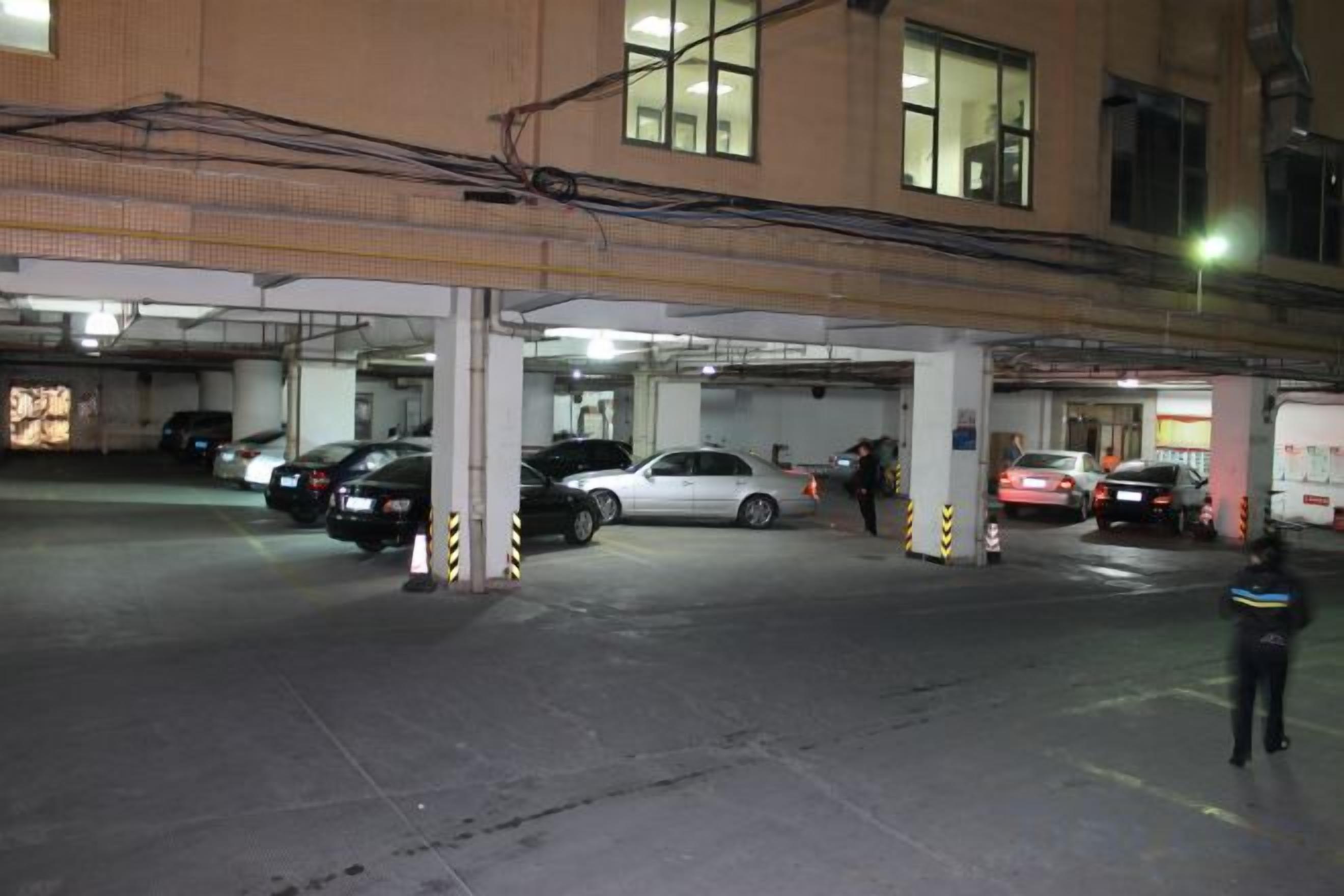 Un estacionamiento de varios niveles con varios coches aparcados, pilares de hormigón y pasarelas superiores.