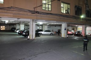 Un estacionamiento de varios niveles con varios coches aparcados, pilares de hormigón y pasarelas superiores.