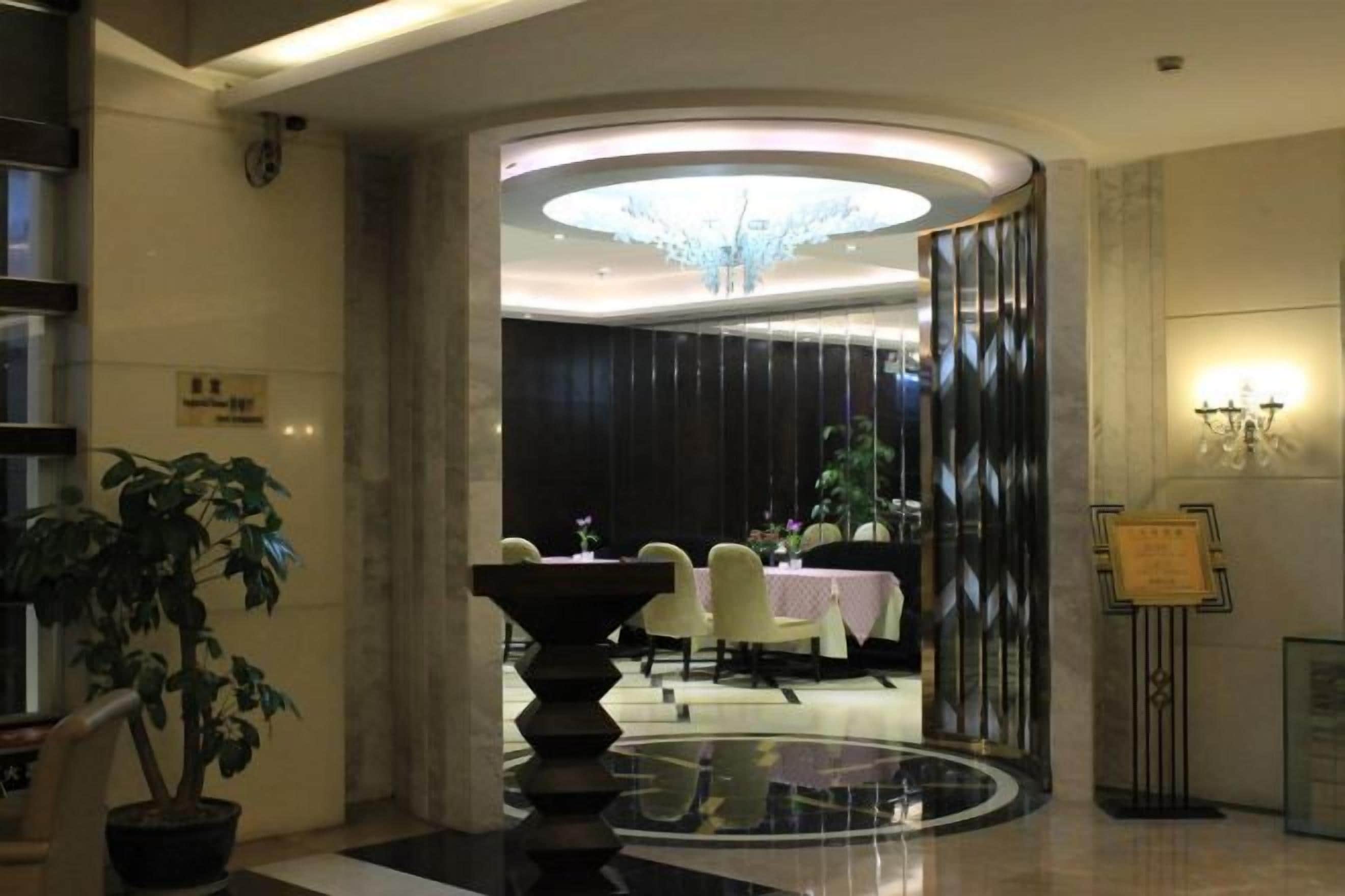 Um saguão de hotel com uma mesa redonda, cadeiras, um candelabro e um vaso de planta.