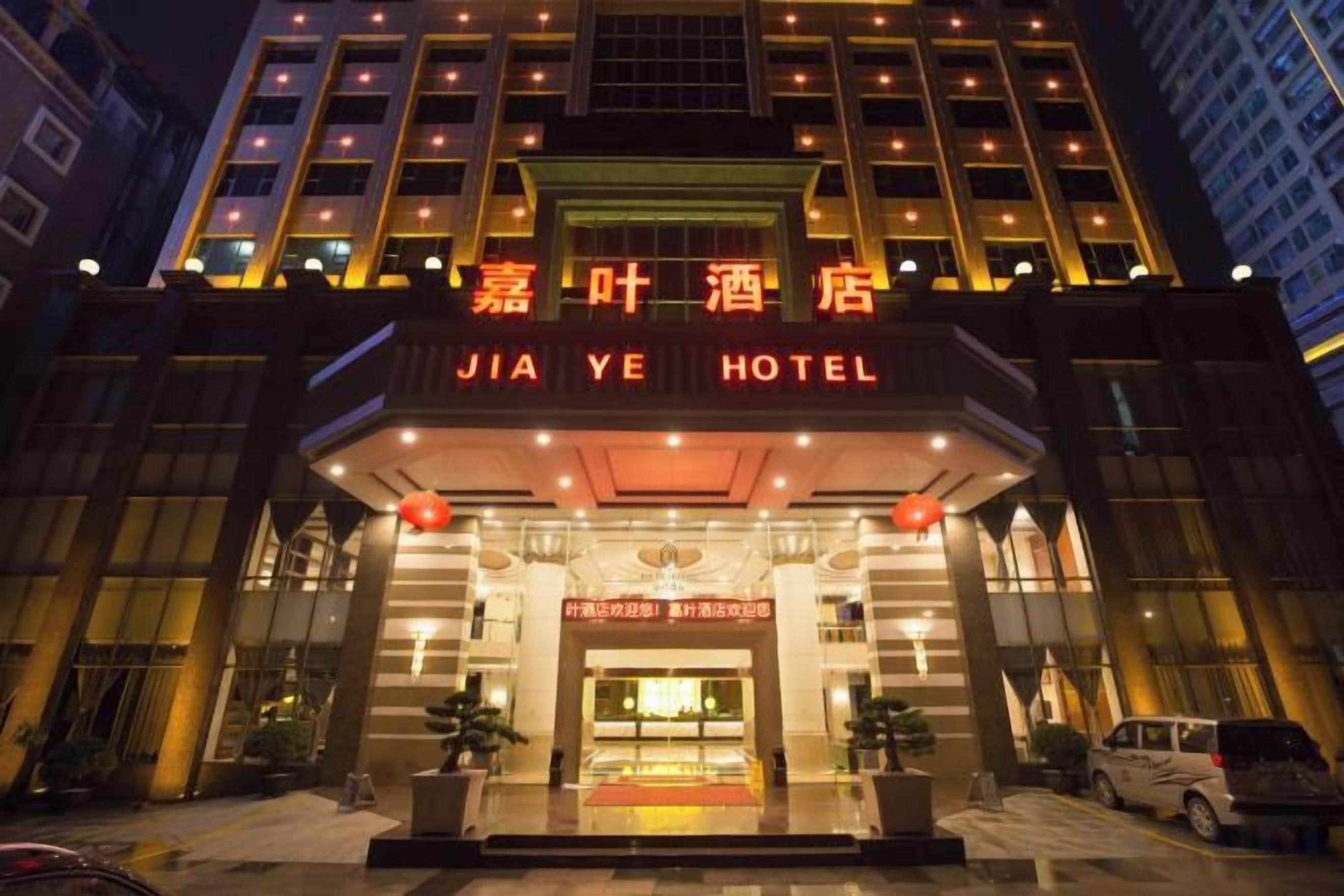 A hotel entrance with illuminated signage, a red lantern, and a car parked in front.