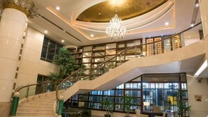 Un amplio vestíbulo con una imponente escalera, una araña de cristal y una gran planta de interior.