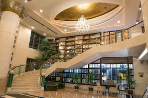 Un amplio vestíbulo con una imponente escalera, una araña de cristal y una gran planta de interior.