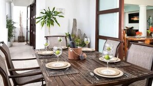 Un coin repas avec une table en bois dressée pour six personnes, entourée de chaises en osier.