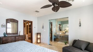 Une chambre à coucher comprenant un lit, une armoire, un miroir, un ventilateur de plafond, et une salle de bain visible à travers une porte ouverte.