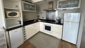 Cocina compacta con armarios blancos, encimera negra, microondas, cafetera y refrigerador.