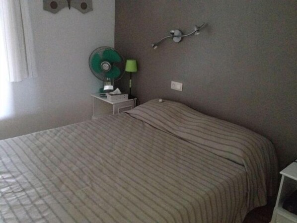 Un dormitorio con cama, mesita de noche con lámpara y una lámpara de pared.