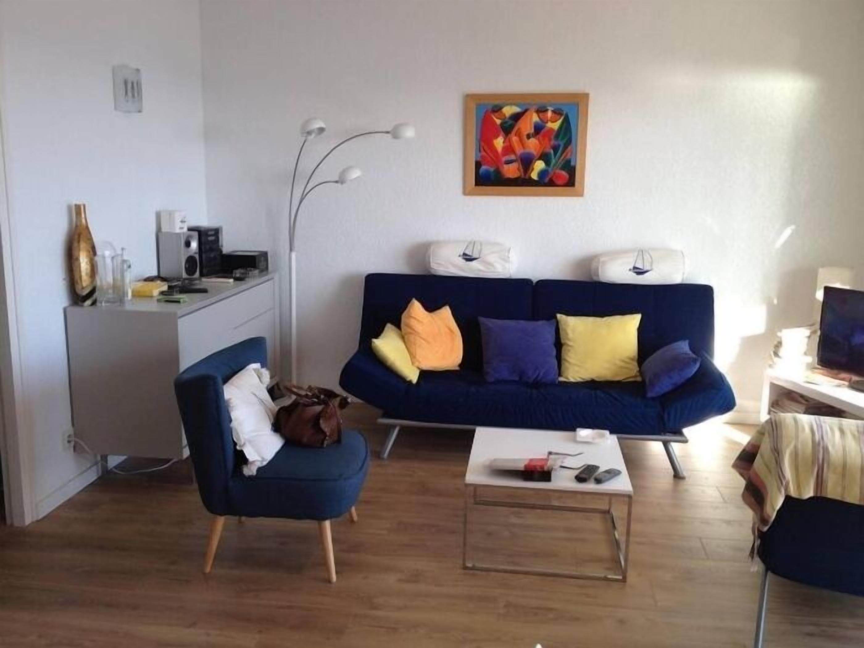 A modern living room with a blue sofa, a coffee table, a desk with a computer, and a painting on the wall.