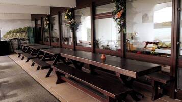 Eine Reihe Holztische mit Bänken, große Fenster mit floralen Verzierungen und ein Blick ins Freie.