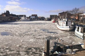 A frozen river with boats docked on the right, buildings in the background, and a clear sky. - Ostseeglück Heiligenhafen – Near beach with lake access (Heiligenhafen)