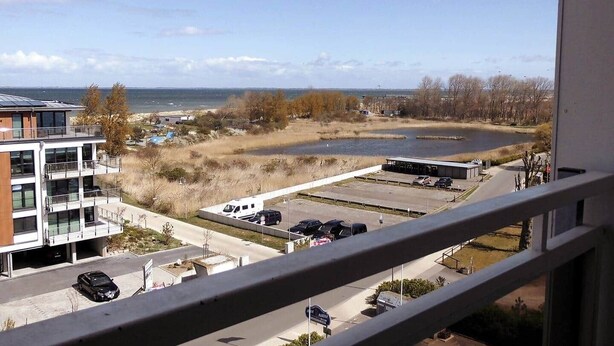 Um edifício moderno com vários andares, uma área de estacionamento com vários carros e vista para um corpo de água e paisagem distante.