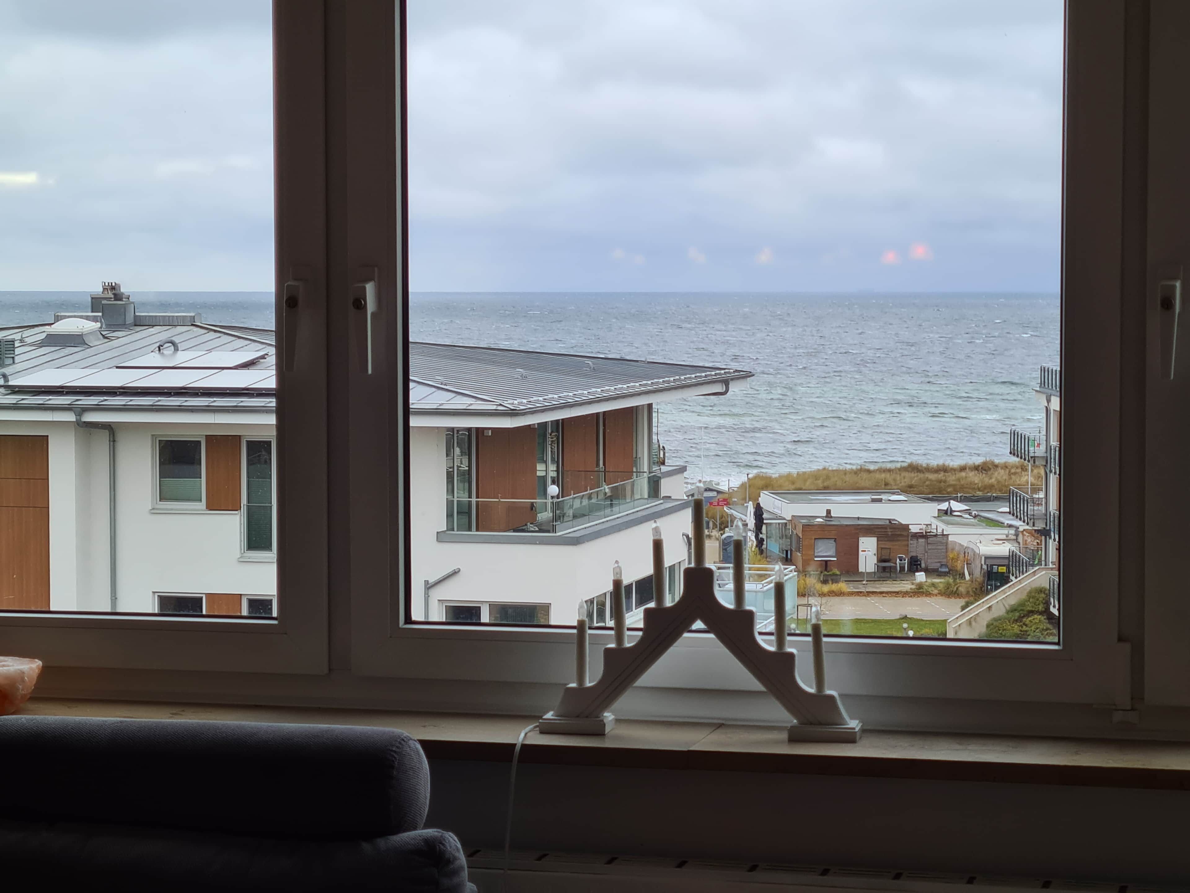 Une vue à travers la fenêtre d’un bâtiment à l’architecture moderne, doté d’un balcon et offrant une vue sur la mer.