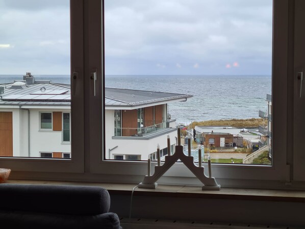 A view through a window of a building with a modern design, featuring a balcony and a view of the sea.