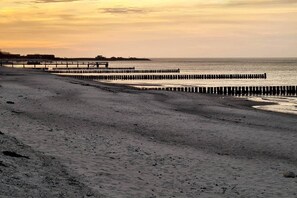 A beach with a wooden pier extending into the water, a sandy shore, and a clear sky.