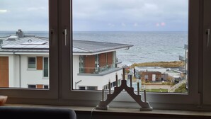 Visão pela janela de um edifício com design moderno, com varanda e vista para o mar.