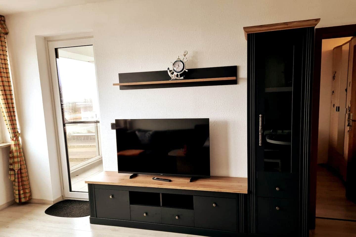 Ein Wohnzimmer mit Fernseher auf Holzständer, Regal darüber und einem Kleiderschrank zur Rechten.