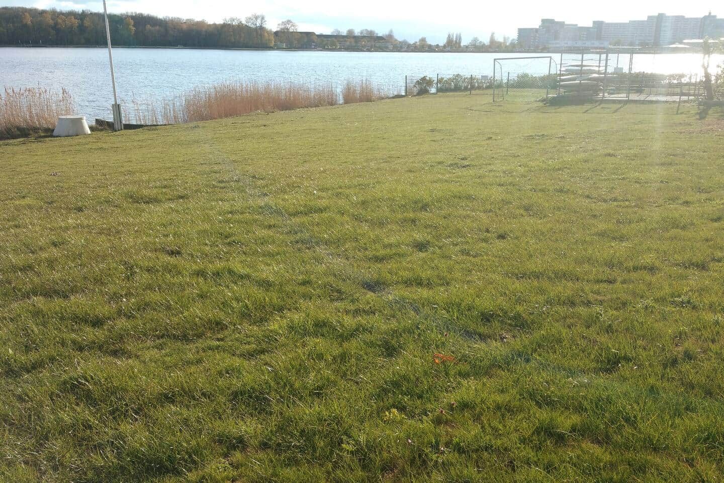 A grassy field with a water body and a sports goal in the background.