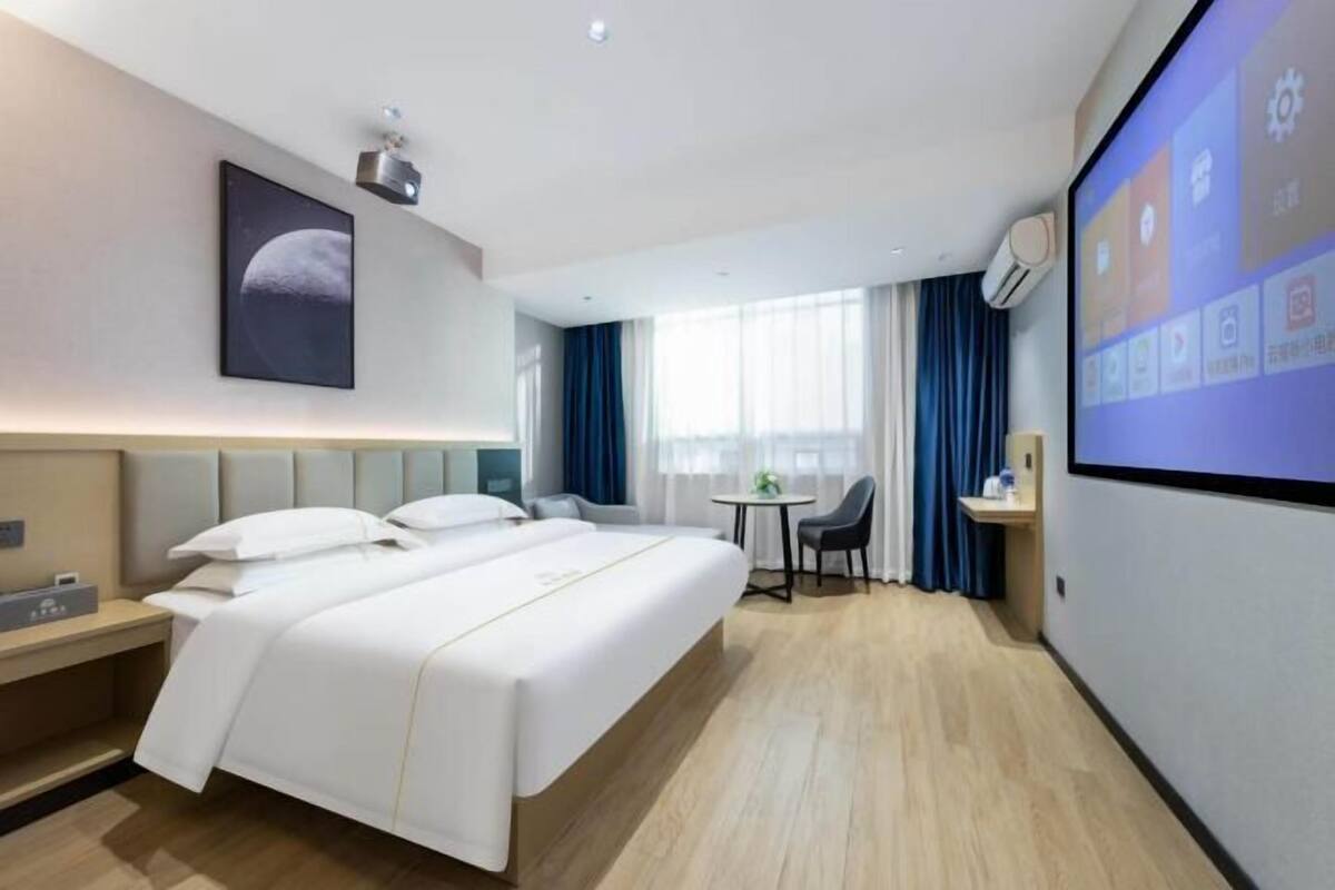 A hotel room with a bed, a desk, a chair, a TV, and a window with curtains.